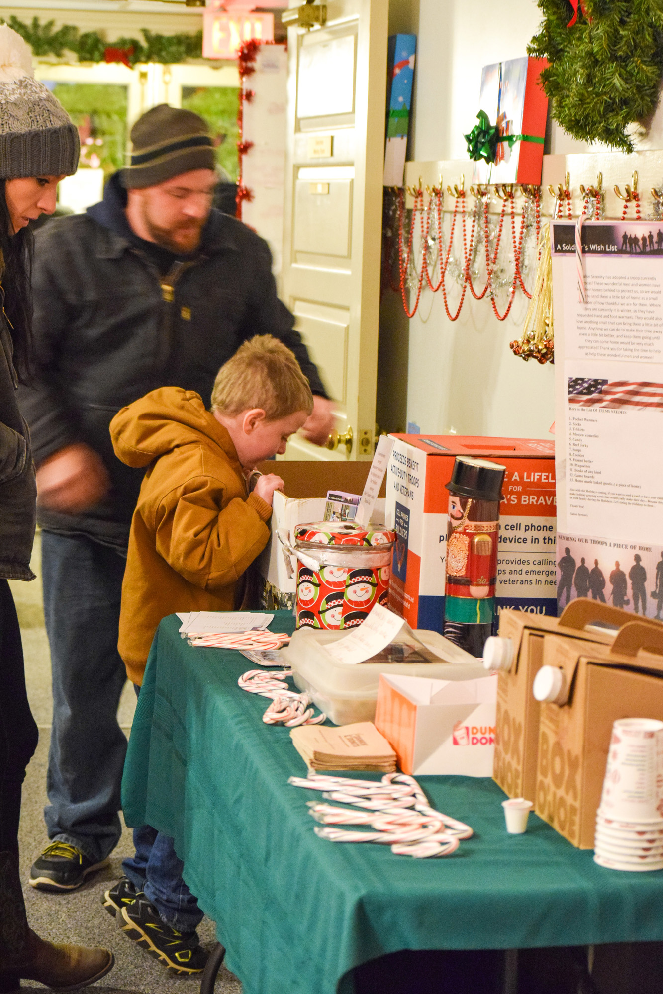 Colin Greenwood, 5, of Halifax helps Rob Firlotte place donations in the collection box at the Salon Serenity cards and care packing station for soldiers overseas as mom Jenni Greenwood (left) looks on.